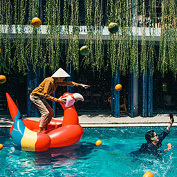 A man riding an inflatable parrot in a swimming pool.